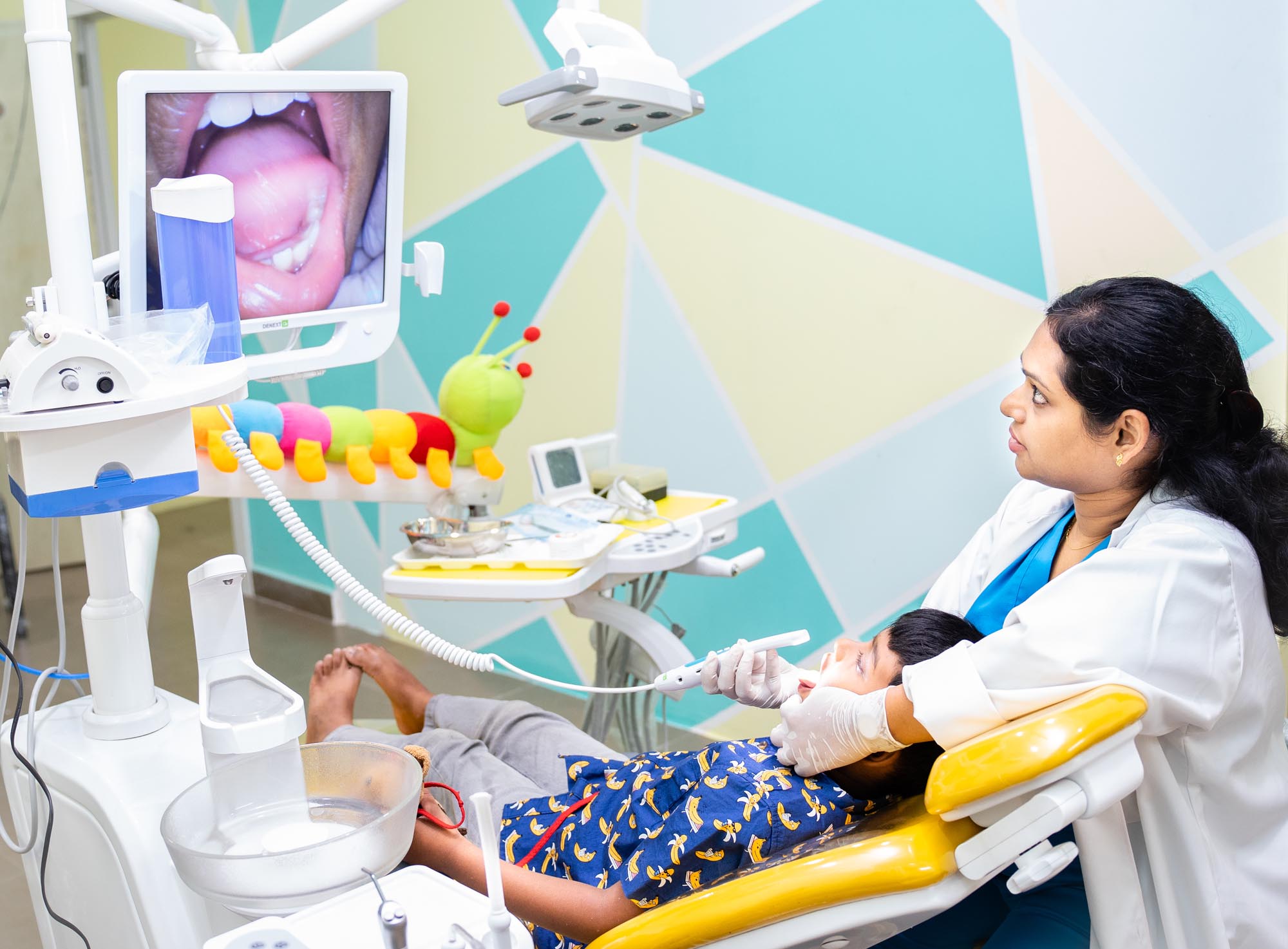 Dr. Sangeeta examining a child's teeth using an intraoral camera, whose images are displayed on a screen.